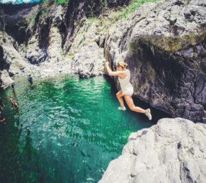 Woman jumping from a rock into a blue lagoon.